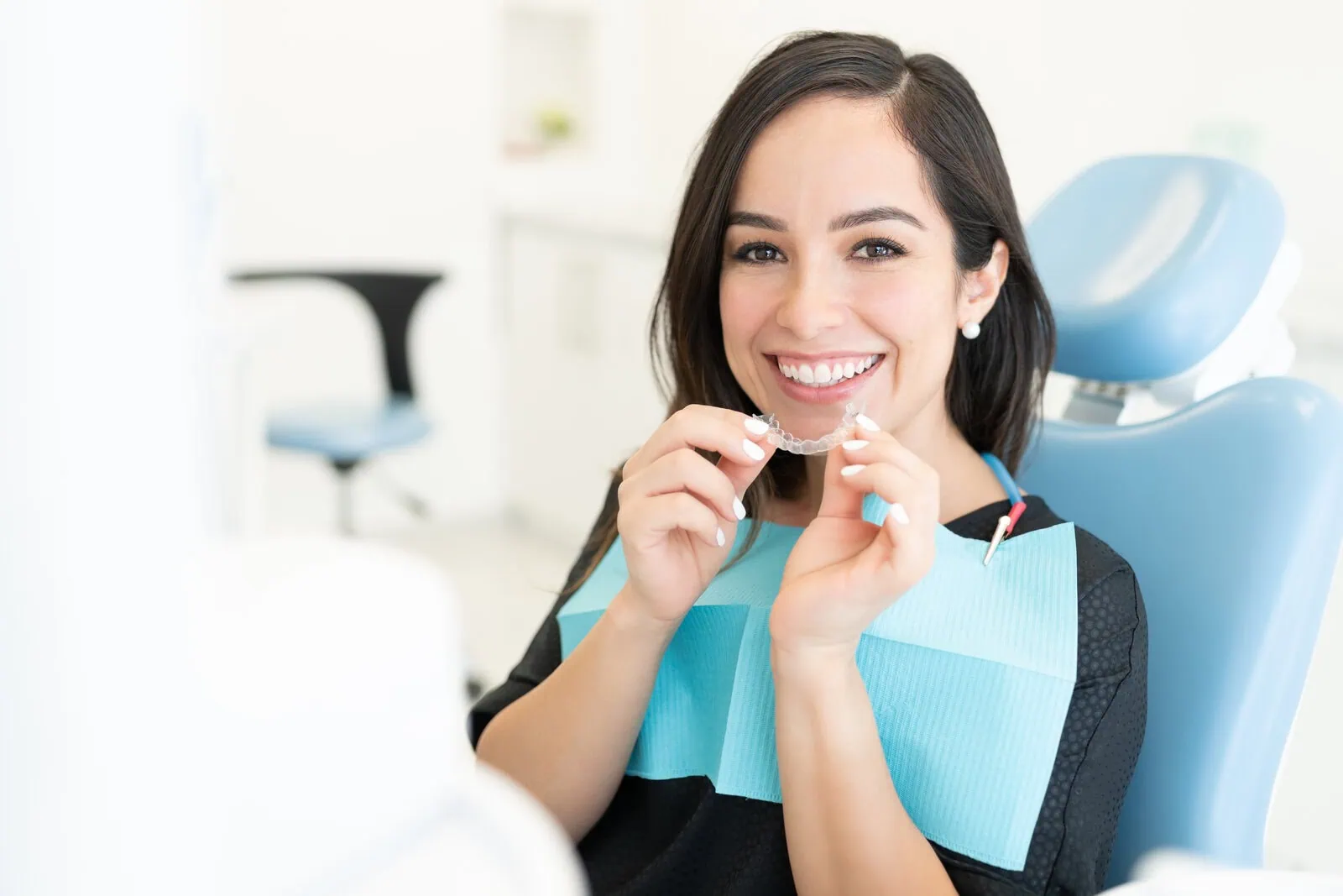 Smiling patient in the treatment chair holding a clear aligner tray